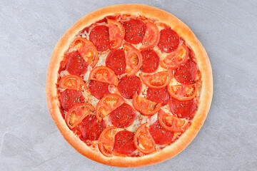 Top view of pepperoni pizza with fresh tomato slices and herbs on gray background. Italian fast food concept