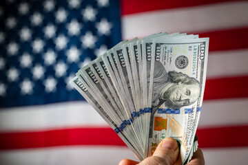Stack of american hundred dollar bills in a hand against the background of the american flag, closeup. Concept of finance, business, economics and reliability of money