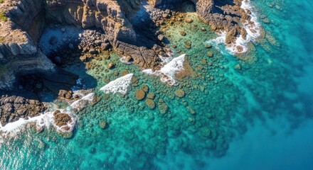 Aerial view of crystal clear turquoise ocean water and rocky shoreline in sunlight