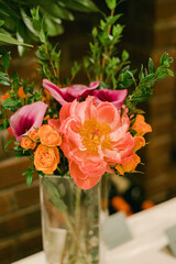Bright floral arrangement featuring pink peonies, orange roses, and greenery in a glass vase on a wooden background