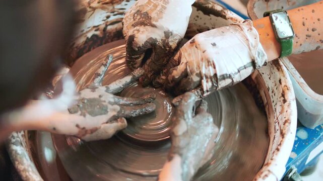 Close up of teacher guiding student hands on spinning pottery wheel. Workshop training in ceramic art, handcraft, traditional clay shaping, artisan skill, authentic learning process, craft education.
