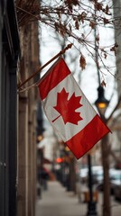 Canadian flag waving gently in the breeze, displayed on a building exterior, surrounded by urban scenery and soft winter light, symbolizing national pride and identity