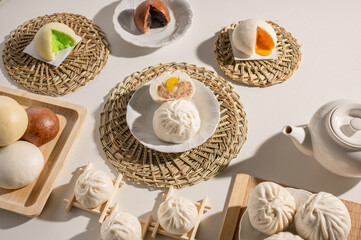 A beautifully arranged display of various steamed buns and a teapot on woven mats, showcasing delightful textures and colors.