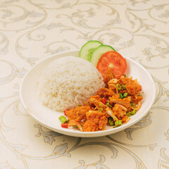 A plate featuring fried chicken with rice, garnished with cucumber and tomato slices on an elegant tablecloth.