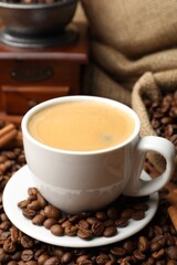 Cup of hot coffee, beans, grinder and cinnamon on brown background, closeup