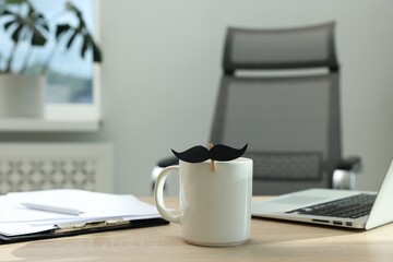 Happy Father's Day. Cup with paper moustache, clipboard and laptop on wooden table