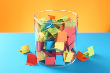 Bright paper pieces in glass jar on color background, closeup