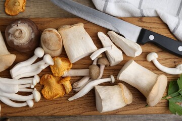 Different raw mushrooms and knife on wooden table, flat lay