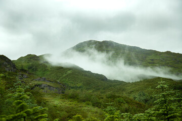 paisaje de montañas cubiertas de verde con niebla en la cima típico de paisajes de Escocia