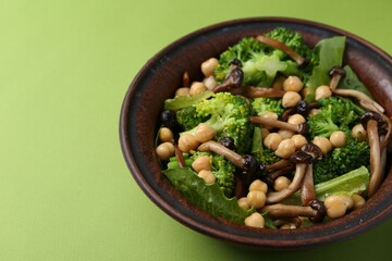 Delicious salad with shimeji mushrooms, chickpeas and broccoli in bowl on green background, closeup. Space for text