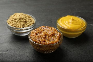 Different types of mustard on black table, closeup