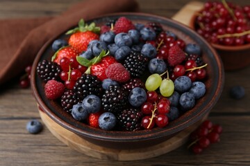 Different ripe berries in bowl on wooden table, closeup