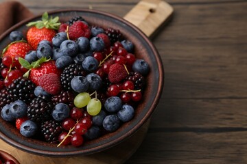 Different ripe berries in bowl on wooden table, closeup. Space for text