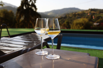 Obraz premium Glasses of wine on sun lounger near swimming pool outdoors