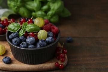 Different ripe juicy berries and basil in bowl on wooden table, closeup. Space for text