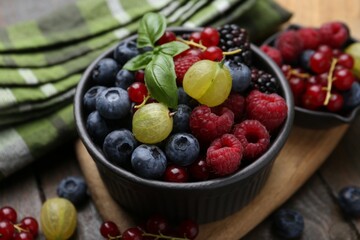 Different ripe juicy berries and basil in bowl on wooden table, closeup
