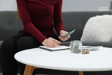 Woman counting dollar banknotes on sofa indoors, closeup