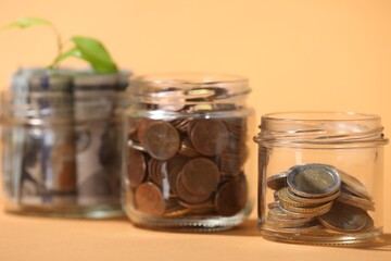 Glass jars with dollars, coins and sprout on pale orange background, closeup