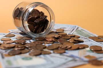Glass jar with coins and dollars on pale orange background, closeup