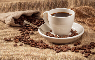 Warm and inviting coffee scene: cup with coffee beans on burlap background
