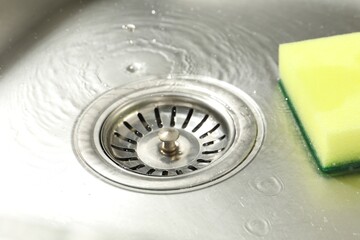 Water going down drain and sponge in sink, closeup