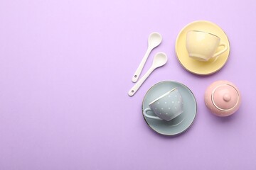 Beautiful ceramic tea set for children on violet background, flat lay. Space for text