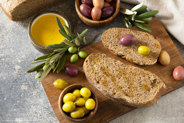 Mediterranean snack with mixed olives, olive oil, and rustic bread on wooden board.