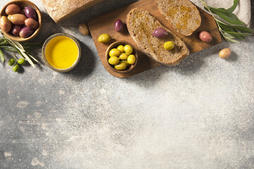 Mediterranean snack with mixed olives, olive oil, and rustic bread on wooden board. Top view.