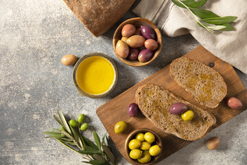 Mediterranean snack with mixed olives, olive oil, and rustic bread on wooden board. Top view flat lay background. Copy space.