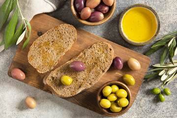 Mediterranean snack with mixed olives, olive oil, and rustic bread on wooden board.