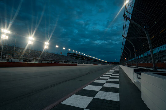 Empty race track at dusk with stadium lights and checkered finish line racing speedway