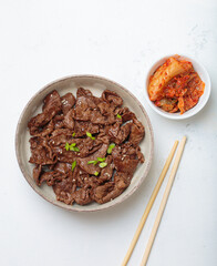 Roasted beef slices Bulgogi, traditional dish of Korea, garnished with sesame seeds and spring onions, served with traditional kimchi on a light table top view