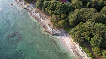 Aerial drone view of a rocky beach coastline in Istria, Croatia, with crystal clear turquoise water, surf waves, stone steps to the shore, and lush green forest above the cliffs. - Powered by Adobe