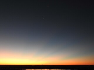 Obraz premium The vibrant colors of an early dawn, with the moon and venus, the morning star, in the sky. Tranquil, colorful scene, Bombay Hook National Wildlife Refuge, Kent County, Delaware.
