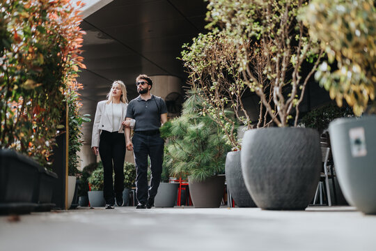 A couple elegantly dressed walking through a garden-like environment amid potted plants. - Powered by Adobe