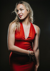 Naklejka premium Elegant woman in a form-fitting red dress posing under soft dramatic studio lighting. Capturing a moment of poise and confidence, showcasing fashion and beauty in an inspiring setting.