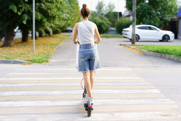 Woman rides electric scooter through crosswalk on sunny day in urban park