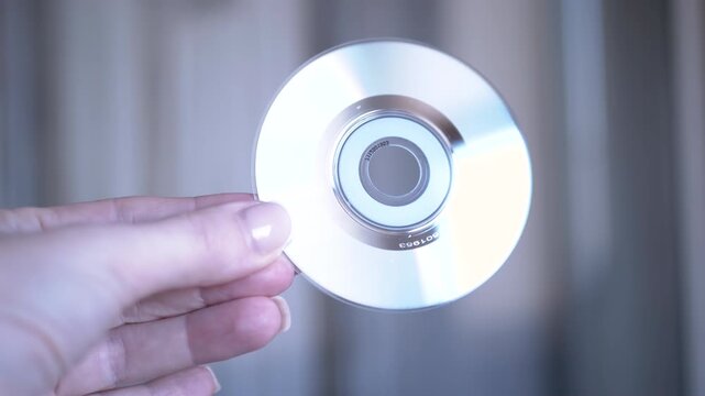 Close-up of a hand holding a blank CD, highlighting the disc's reflective surface and the details of the hand.