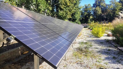 Modern solar panels installed in a garden, surrounded by green trees and plants, under bright sunlight on a clear day