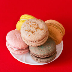 5 pastel-colored macaroons stacked on a white plate on a bright red background