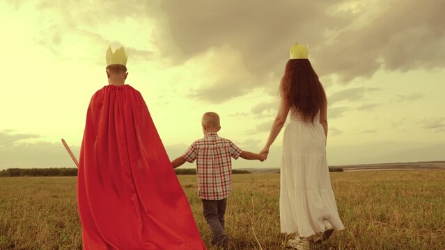 happy family. boy son with mother plays red cape superhero meadow. happy family concept. chidhood dream. golden crown on his head. child dream kid protect help group people. teamwork. fantastic game