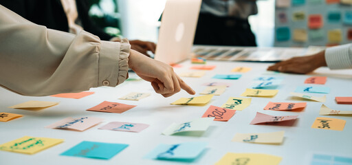 A group of professionals engages in a collaborative brainstorming session, using colorful sticky notes for idea generation and strategy planning at a modern office desk. SACTR