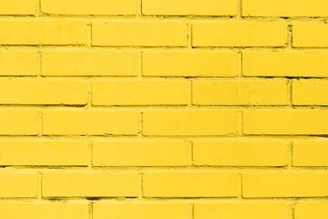 Obraz premium Yellow painted brick wall background. Urban surface with vibrant color. Industrial construction with texture and pattern. Simple geometry of rectangular bricks. Design element for architecture.