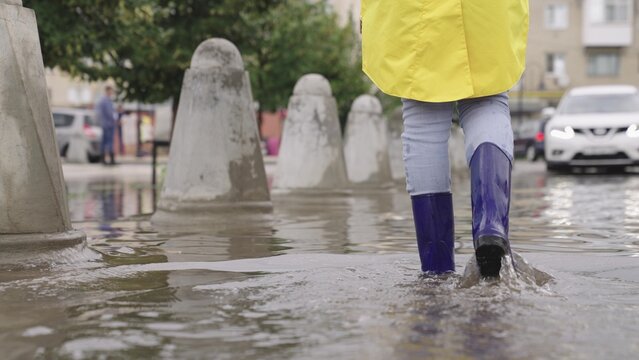 girls in rubber boots are walking in a puddle, a flood on a city street, flood on the sides of roads and asphalt roadway, splashes different directions from wet muddy puddle, presence water districts.