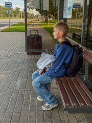 Blonde teenage boy sitting at bus stop waiting for bus