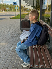 Blonde teenage boy sitting at bus stop waiting for bus