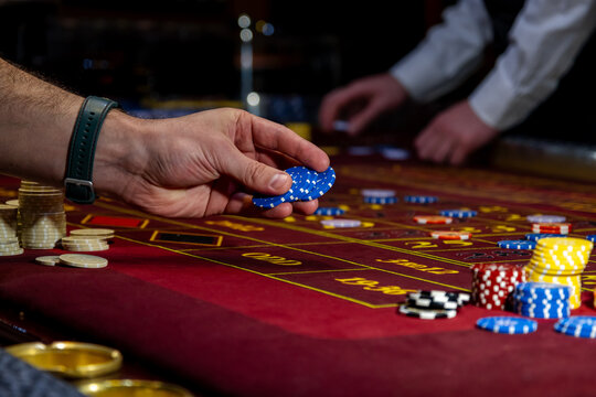 Man playing at the roulette table. A close-up vibrant image of multicolored casino table with roulette in motion, with casino chips. the hand of croupier.