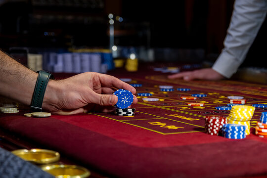 Man playing at the roulette table. A close-up vibrant image of multicolored casino table with roulette in motion, with casino chips. the hand of croupier.