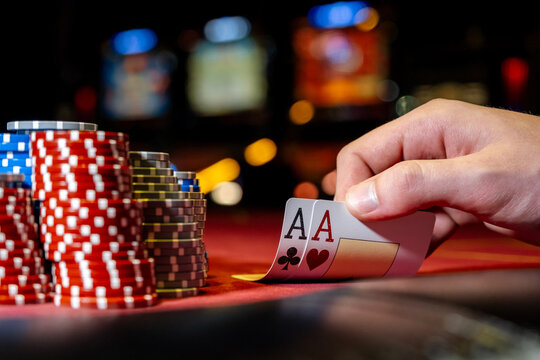 Player opens playing cards with one pair or two aces on red poker table. Close-up of playing chips and hand with cards on table in club or casino.