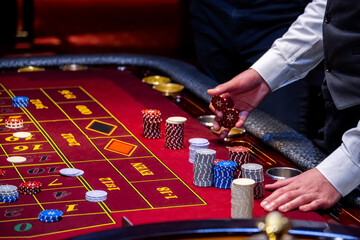 Croupier behind gambling table in a casino. Roulette wheel and croupier hand. A player in a casino,...